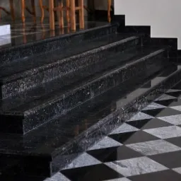 Polerowane, czarne schody z granitu z widocznymi ziarnami, prowadzące do góry, z podłogą w czarno-białą szachownicę.