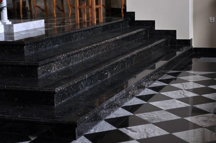 Polerowane, czarne schody z granitu z widocznymi ziarnami, prowadzące do góry, z podłogą w czarno-białą szachownicę.