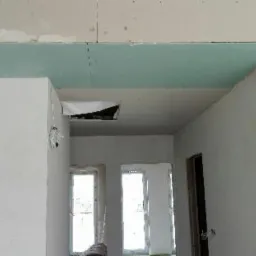 Wnętrze w trakcie prac wykończeniowych: sufit z płyt kartonowo-gipsowych, widoczne łączenia płyt, ściany przygotowane do malowania, otwór instalacyjny w suficie.