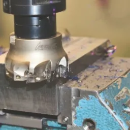 Frezarka CNC w trakcie obróbki metalowego elementu, widoczne wióry i chłodziwo.