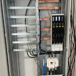 Wnętrze szafy sterowniczej z szynami miedzianymi, bezpiecznikami i okablowaniem, widoczne elementy montażowe i podłączenia elektryczne.