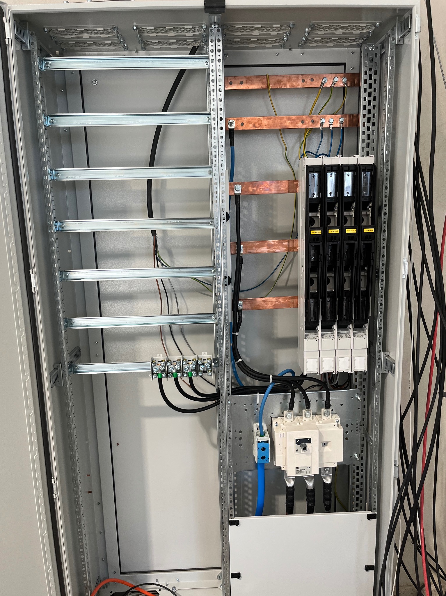 Wnętrze szafy sterowniczej z szynami miedzianymi, bezpiecznikami i okablowaniem, widoczne elementy montażowe i podłączenia elektryczne.
