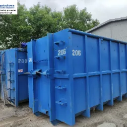 Dwa niebieskie, puste kontenery z numerami 203 i 206 stoją obok siebie na placu. Widoczne logo firmy PBI Częstochowa na jednym z kontenerów. W tle drzewa i budynek.