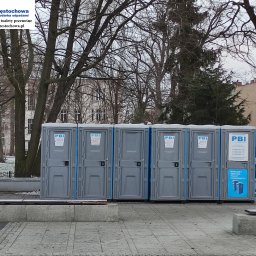 PBI Spółka Jawna - Szereg szarych, przenośnych toalet z niebieskimi akcentami, ustawionych na chodniku w miejskim otoczeniu, z widocznymi budynkami w tle i drzewami bez liści, sugerującymi porę zimową.