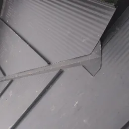 Szczeg&oacute;łowe ujęcie fragmentu czarnego dachu z blachy trapezowej, ukazujące precyzyjne łączenie element&oacute;w i obr&oacute;bki blacharskie w załamaniu połaci.