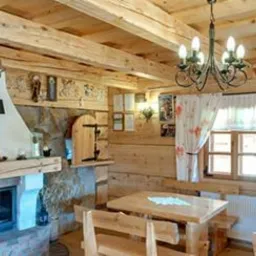 Drewniany salon z kominkiem, stołem i krzesłami w rustykalnym stylu, oświetlony żyrandolem z żarówkami świecowymi.