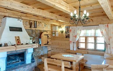 Drewniany salon z kominkiem, stołem i krzesłami w rustykalnym stylu, oświetlony żyrandolem z żarówkami świecowymi.