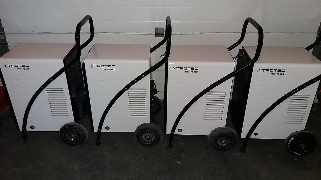 Rząd czterech białych osuszaczy powietrza Trotec TTK 170 ECO z czarnymi uchwytami i kółkami, ustawionych w magazynie.
