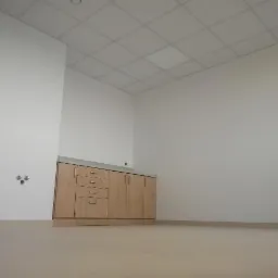 Jasne pomieszczenie z zabudową meblową z drewnopodobnymi frontami i szarym blatem, widoczne gniazdka elektryczne w ścianie.