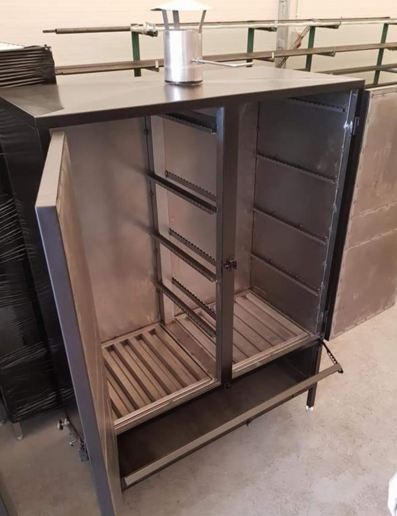 Otwarta, metalowa konstrukcja szafy wędzarniczej z półkami, widoczne elementy spawane, komin na górze, surowe wykończenie.