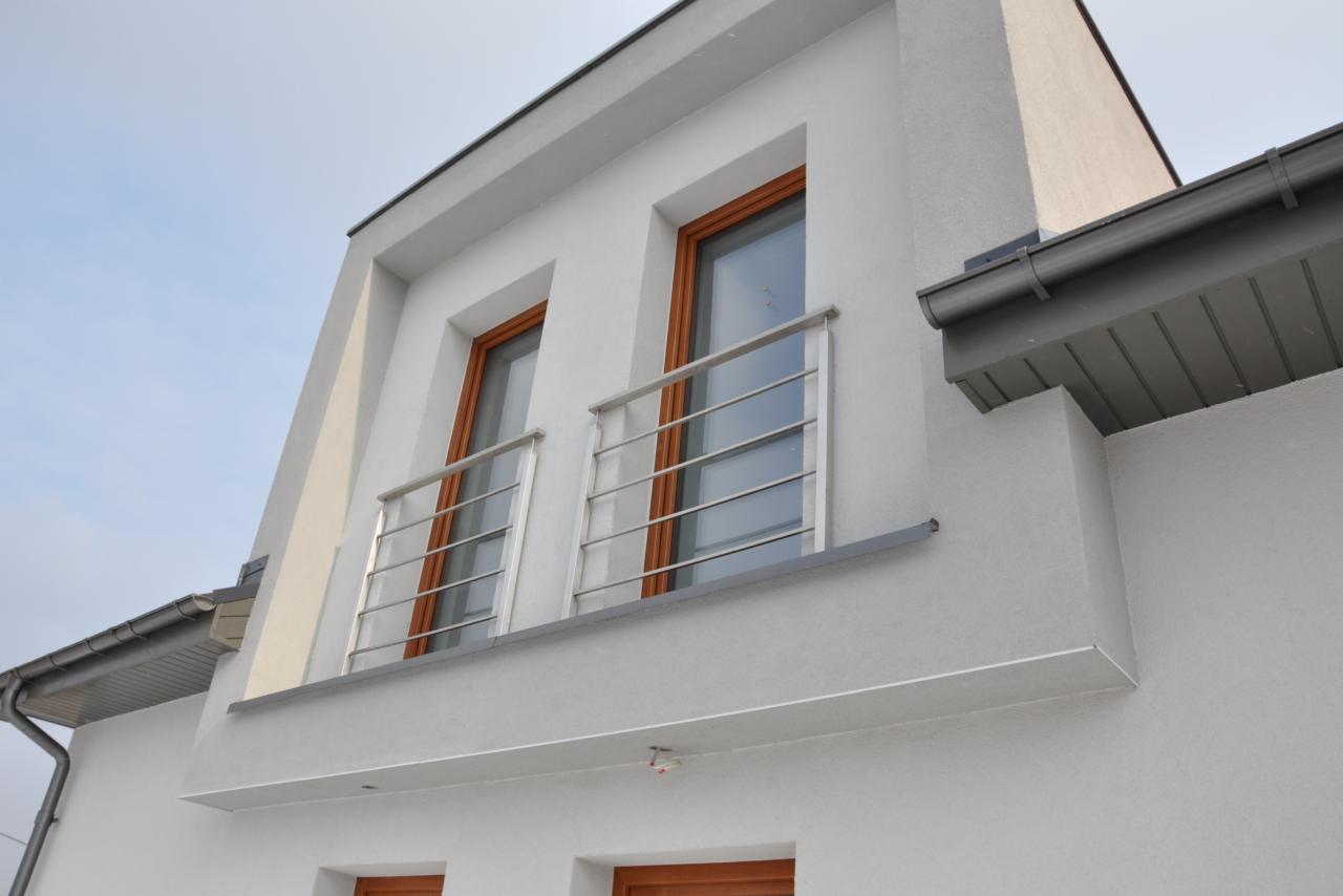 Fragment elewacji budynku z dwoma oknami z drewnianymi ramami i srebrnymi balustradami balkonowymi, widok z dołu.