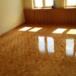 Błyszcząca, świeżo polakierowana podłoga parkietowa ułożona we wzór jodełki, z widocznymi refleksami światła słonecznego wpadającego przez okna.