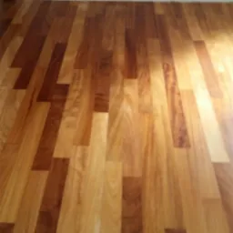 Ułożona podłoga z parkietu o zróżnicowanym odcieniu drewna, widoczne połączenia klepek i fragment ściany z gniazdkiem elektrycznym.