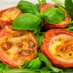 Pieczone pomidorki z mozzarellą bez laktozy na liściach szpinaku i bazylii.