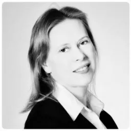 Portret kobiety w czarno-białej tonacji, ubranej w koszulę z kołnierzykiem i marynarkę, z delikatnym uśmiechem, prawdopodobnie przedstawicielki firmy konsultingowej ze Świdnicy.