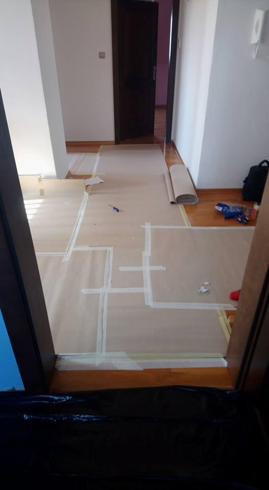 Przygotowanie podłoża w Szczecinie: Parkiet zabezpieczony kartonem i taśmą malarską przed dalszymi pracami wykończeniowymi, widoczny fragment rolki kartonu i narzędzia.