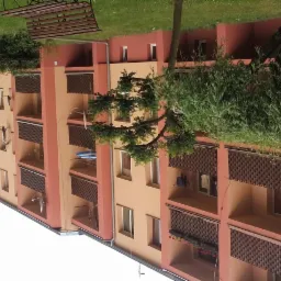 Wielopiętrowy budynek mieszkalny z balkonami zabezpieczonymi ażurowymi osłonami, świeżo pomalowany na odcienie brzoskwini i terakoty, z widocznymi antenami satelitarnymi i elementami suszącej się...