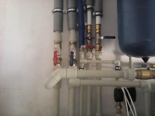 Szczegółowe ujęcie instalacji centralnego ogrzewania z rurami z tworzywa sztucznego, zaworami kulowymi z czerwonymi i niebieskimi uchwytami, oraz fragmentem zbiornika wyrównawczego na tle białej...