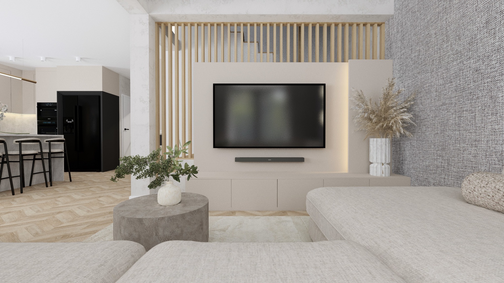 Jasne wnętrze salonu z telewizorem, drewnianą ścianką działową, szarą sofą i okrągłym stolikiem kawowym z wazonem, widok na kuchnię z czarną lodówką i barowymi stołkami.