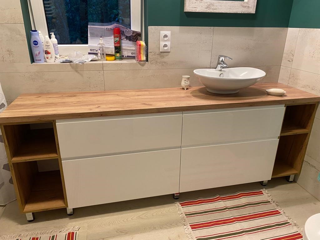Szafka łazienkowa na wymiar z blatem drewnopodobnym, białymi frontami szuflad i otwartymi półkami po bokach, umywalka nablatowa.