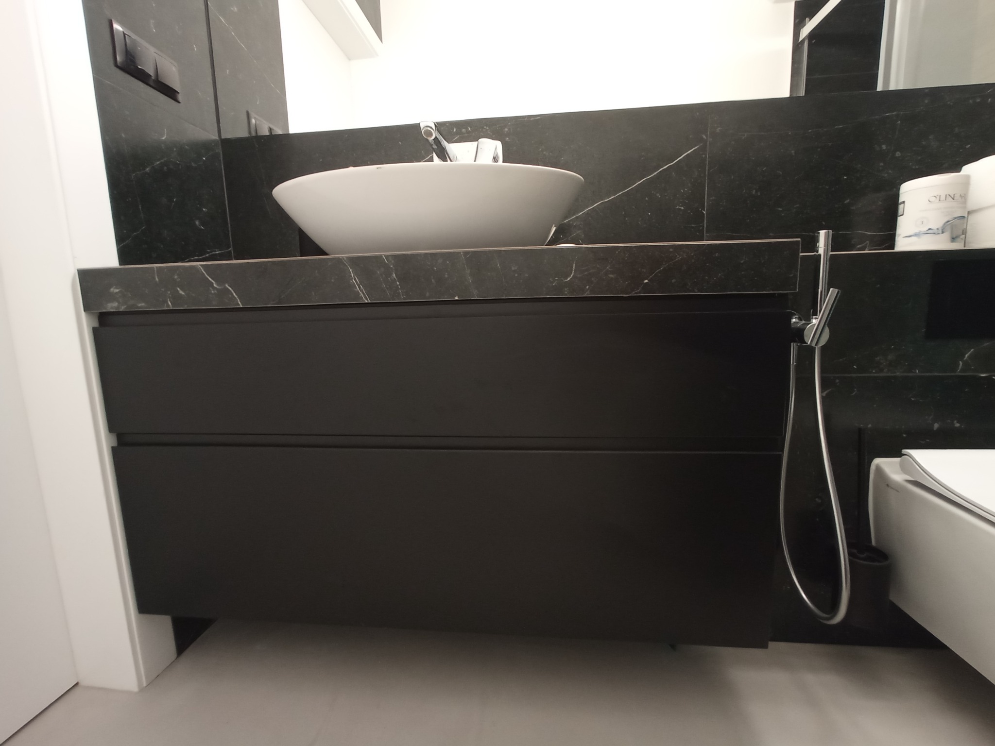 Nowoczesna łazienka z umywalką nablatową, czarnym blatem z marmurowym wzorem i szafką z dwiema szufladami w kolorze grafitowym, białe ściany.
