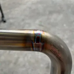 Szczegółowe zbliżenie spawu na złączu rurowym, widoczne charakterystyczne tęczowe przebarwienia termiczne i laserowo naniesione oznaczenia na powierzchni metalu.