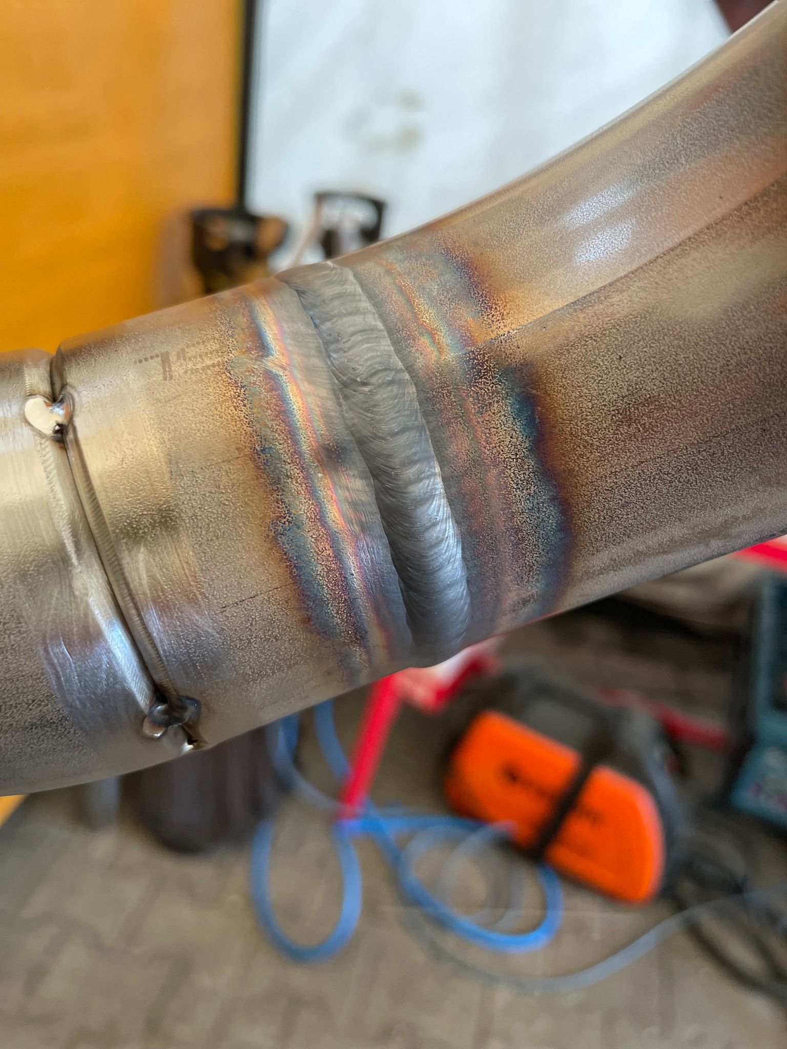 Metalowa rura połączona precyzyjnym spawem, widoczne tęczowe przebarwienia termiczne, w tle narzędzia.