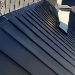 Nowoczesny dach z blachy na budynku z wieżyczką i kominem, widok z góry w słoneczny dzień.