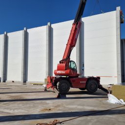 FUH DACHTEX TOMASZ KOWALSKI - Montaż białych płyt warstwowych na hali przemysłowej za pomocą czerwonego podnośnika Manitou. Widoczne materiały izolacyjne Kingspan i pracownik na podnośniku koszowym.