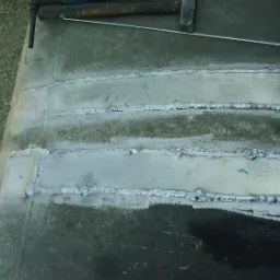 Spoina na metalowej powierzchni, widoczne ślady spawania, młotek i drut spawalniczy w tle.