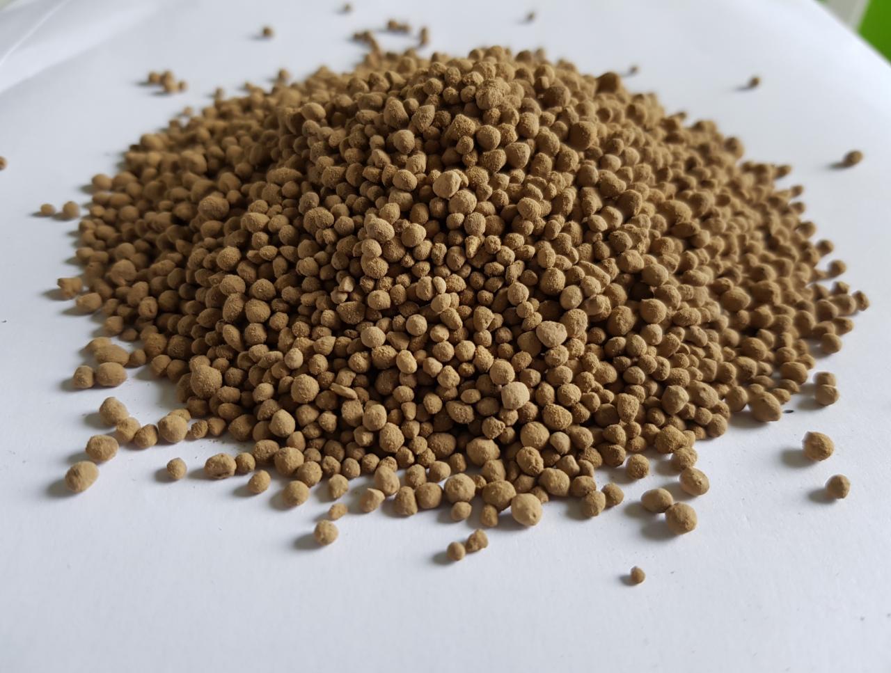 Kopuła brązowych, granulowanych kulek nawozu na białym tle, o nieregularnej powierzchni i widocznych pojedynczych granulkach.