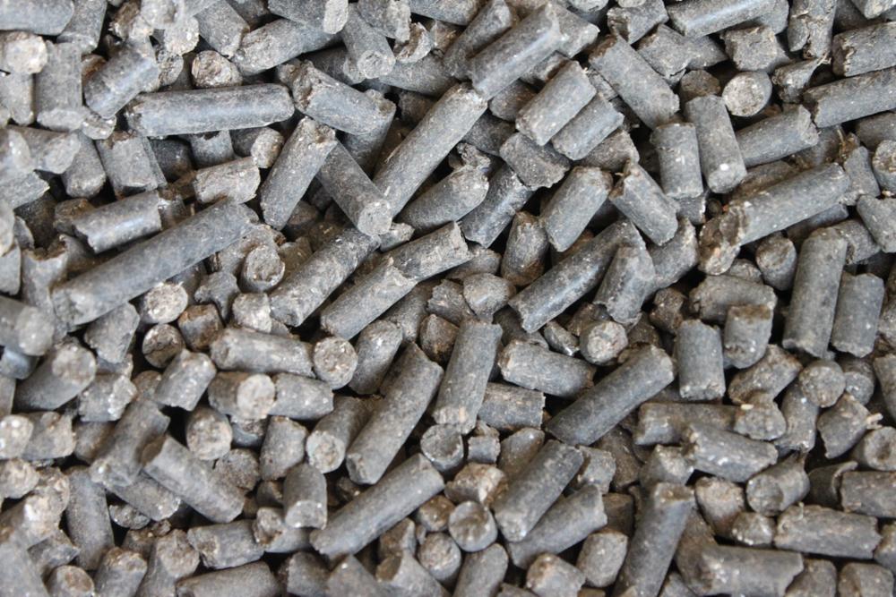 Zbliżenie na szare, cylindryczne granulki nawozu organicznego, z widocznymi nierównościami i pęknięciami, ukazujące ich teksturę i strukturę.