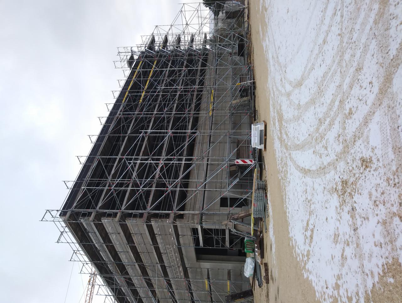 Budynek w trakcie renowacji z licznymi rusztowaniami, widoczne ślady opon na zaśnieżonym gruncie.