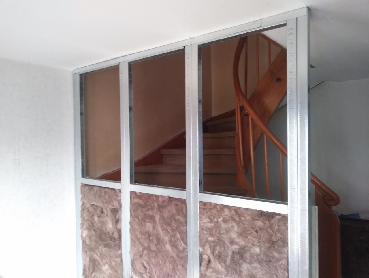 Montaż płyty karton gips z widoczną izolacją z wełny mineralnej oraz fragmentem drewnianych schodów w tle, Barcino.