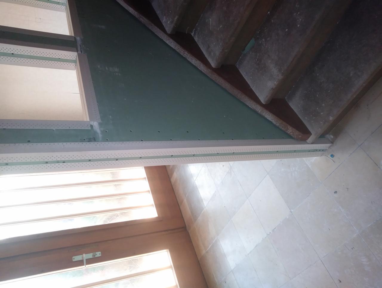 Sufit pod schodami wykończony płytami gipsowo-kartonowymi, widoczne profile narożnikowe i fragment schodów.