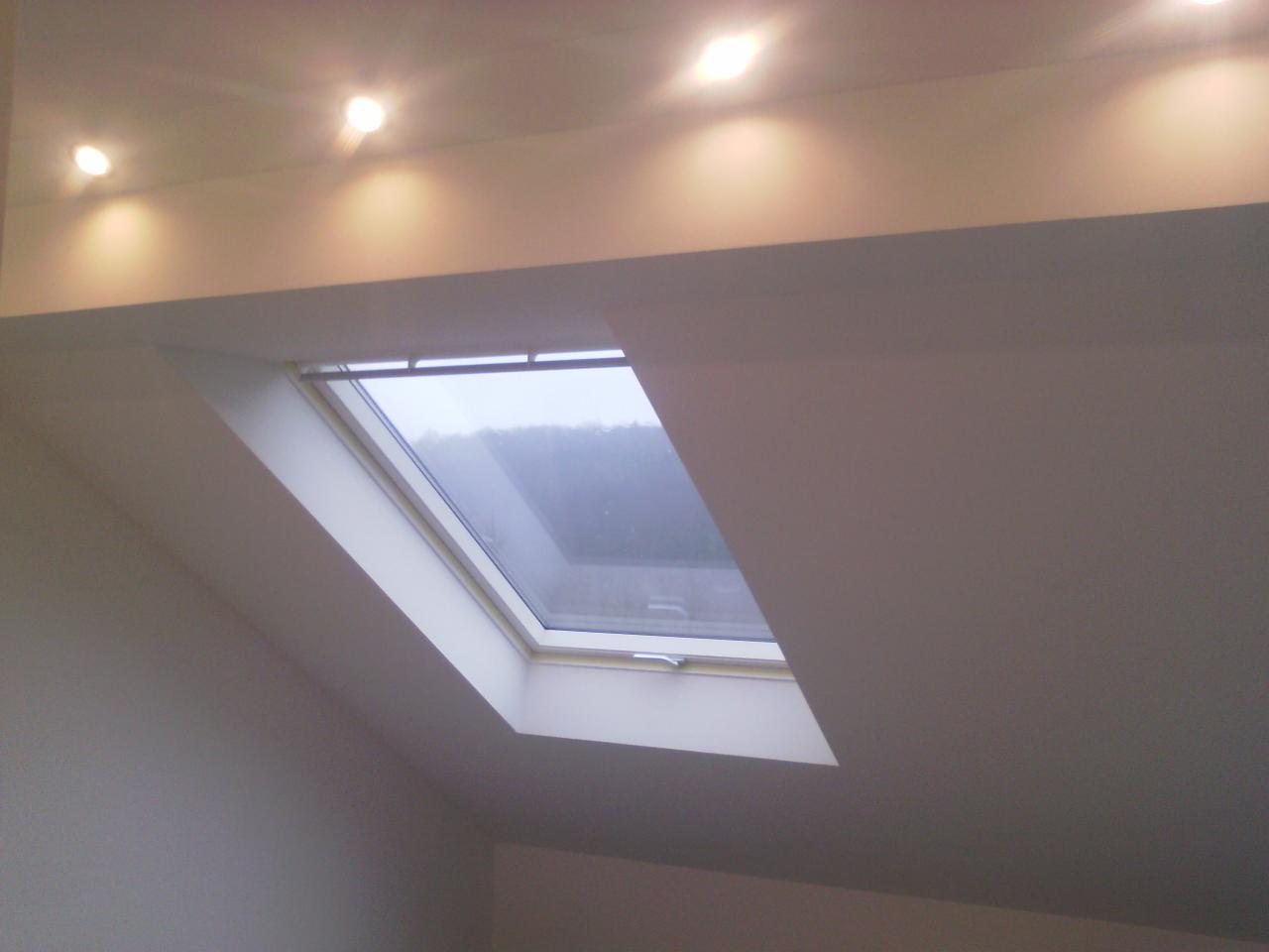 Poddasze z oknem dachowym, widoczne oświetlenie sufitowe, ściany pomalowane na jasny kolor.