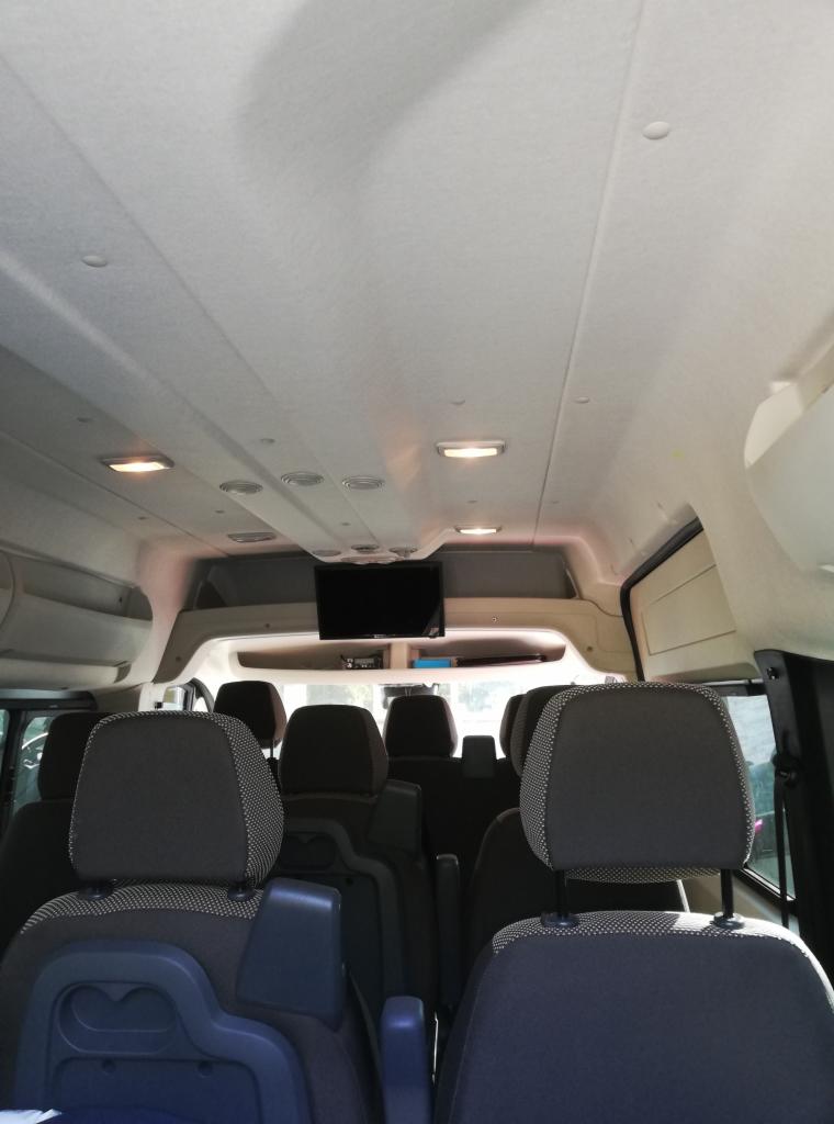 Wnętrze busa pasażerskiego z rzędami foteli, oświetleniem sufitowym i zamontowanym telewizorem.