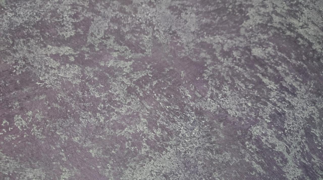 Fioletowa ściana z nieregularną, szarą strukturą przypominającą efekt dekoracyjny, widoczny z bliska.