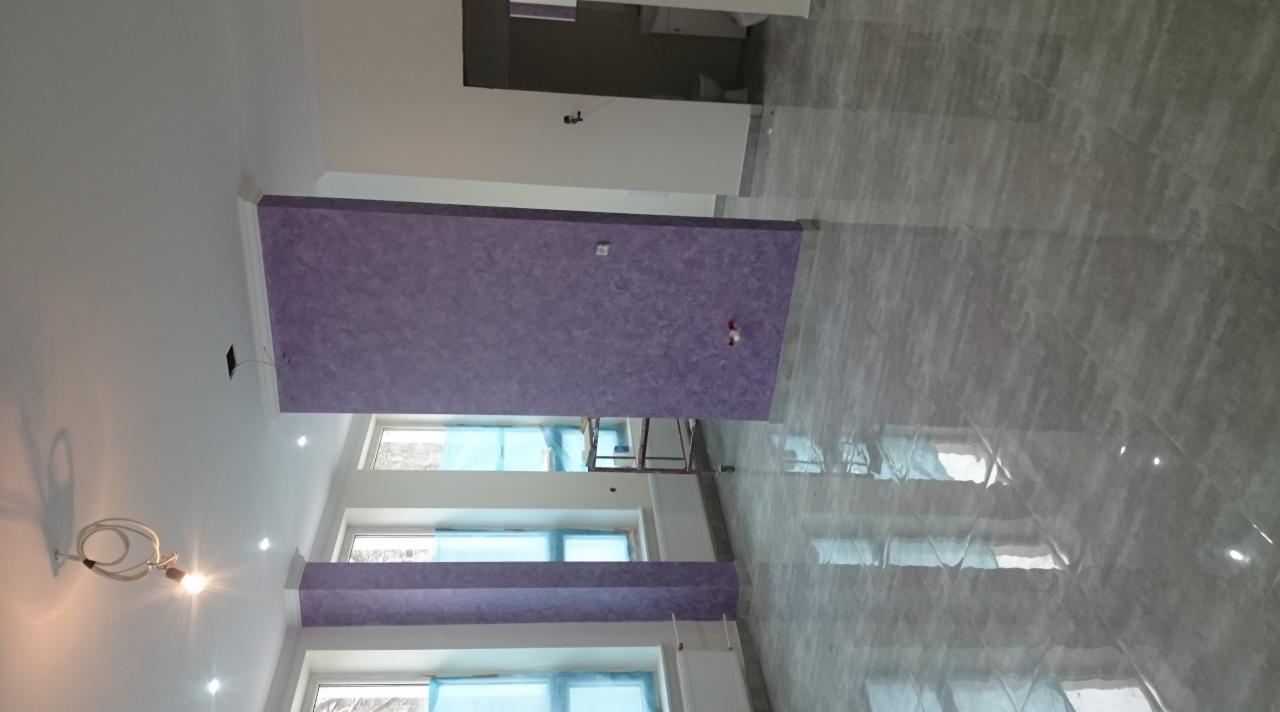 Wnętrze w trakcie wykończenia: ściany z dekoracyjną, fioletową fakturą, zabezpieczone okna folią, błyszcząca, szara podłoga, widoczny fragment rusztowania.