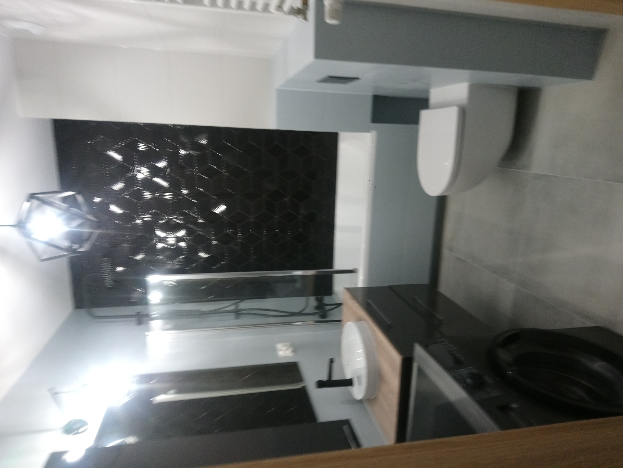 Nowoczesna łazienka w Radomyśl Wielki z czarną, geometryczną mozaiką na ścianie, szarą armaturą i podwieszaną toaletą.