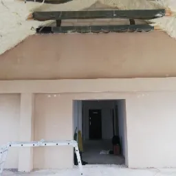 Świeżo otynkowane poddasze z widoczną izolacją piankową, drabina aluminiowa w pomieszczeniu z przygotowanym otworem drzwiowym.