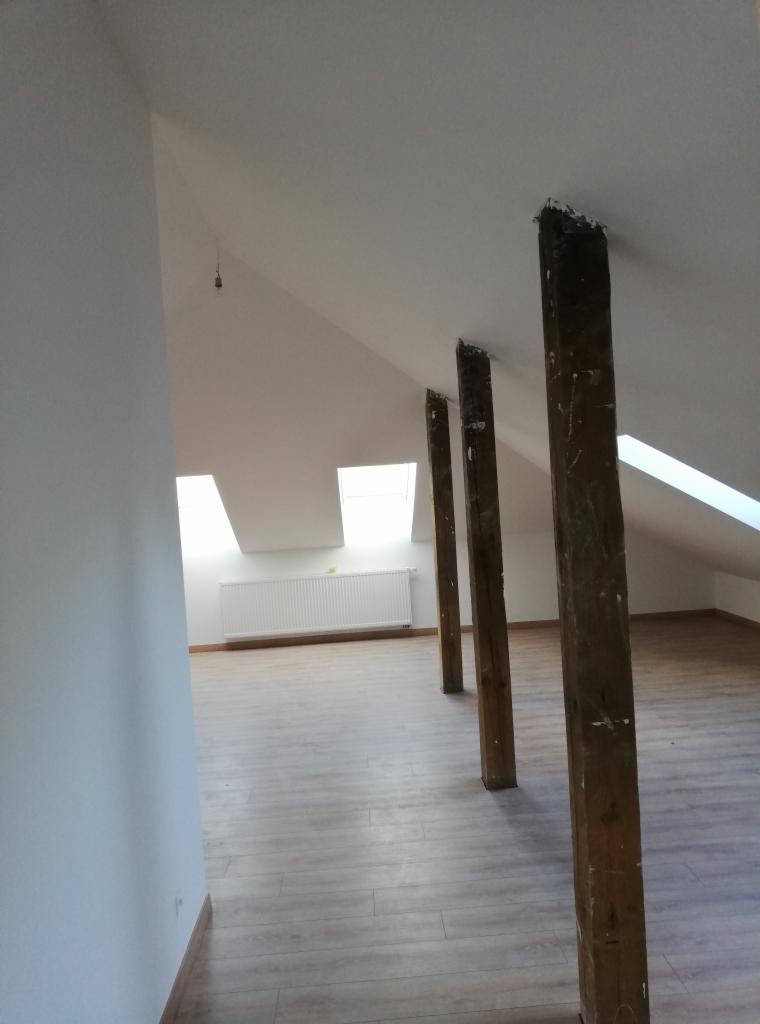 Poddasze po remoncie z drewnianymi słupami konstrukcyjnymi, widoczne okna dachowe, grzejnik i panele podłogowe.