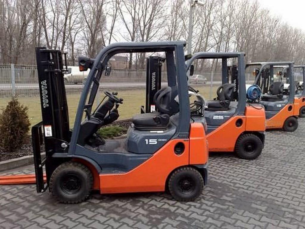 Rząd nowych, pomarańczowo-szarych wózków widłowych marki Toyota, ustawionych na brukowanym placu, z widocznym numerem '15' na pierwszym wózku.
