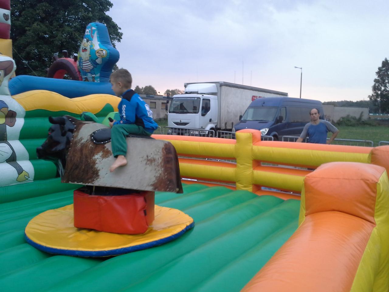 Chłopiec siedzi na dmuchanym byku na tle dmuchanego zamku i pojazdów.