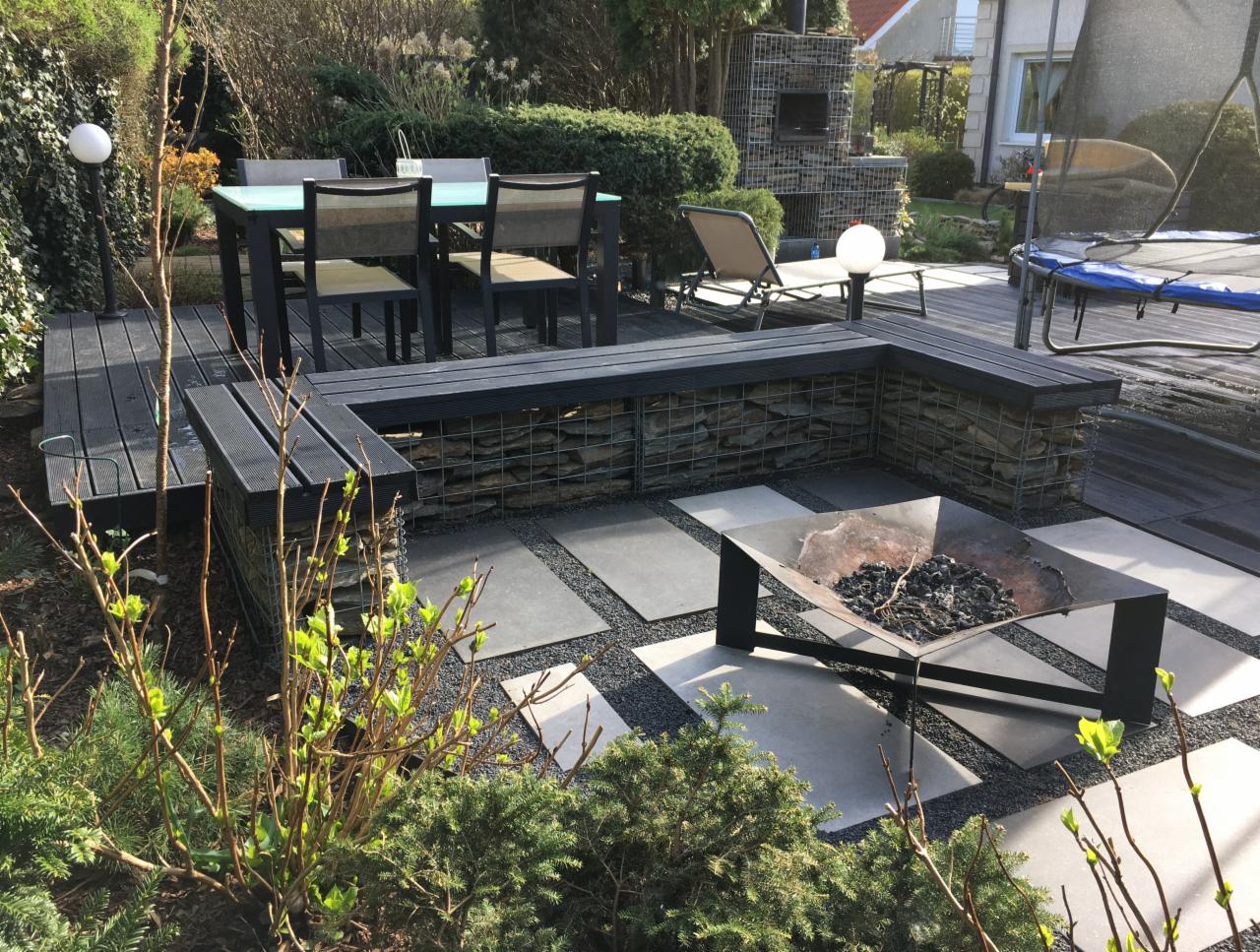 Nowoczesny taras w Miszewku z paleniskiem, meblami ogrodowymi i gabionową ławką, otoczony zielenią.