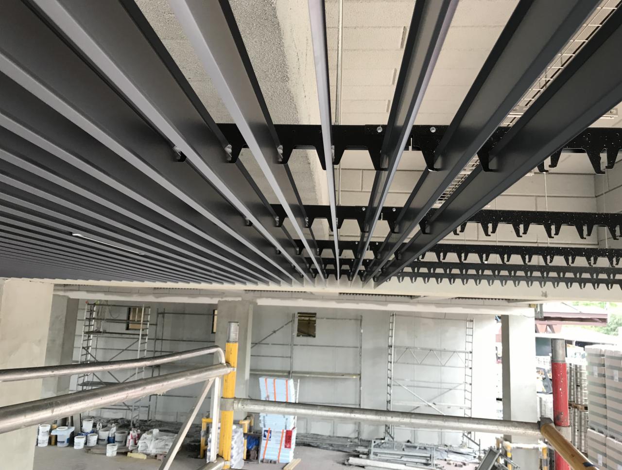 Montaż sufitu rastrowego z widoczną konstrukcją nośną i elementami instalacji w surowym wnętrzu biurowym w trakcie prac wykończeniowych.
