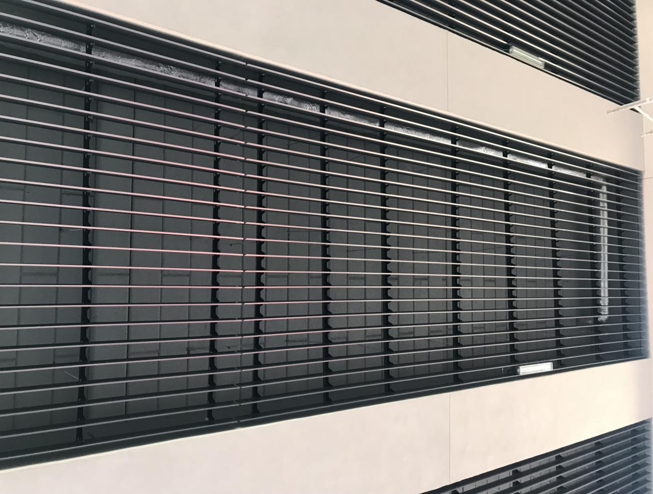 Metalowa konstrukcja sufitowa z poziomymi listwami i oświetleniem, widok z dołu pod kątem.