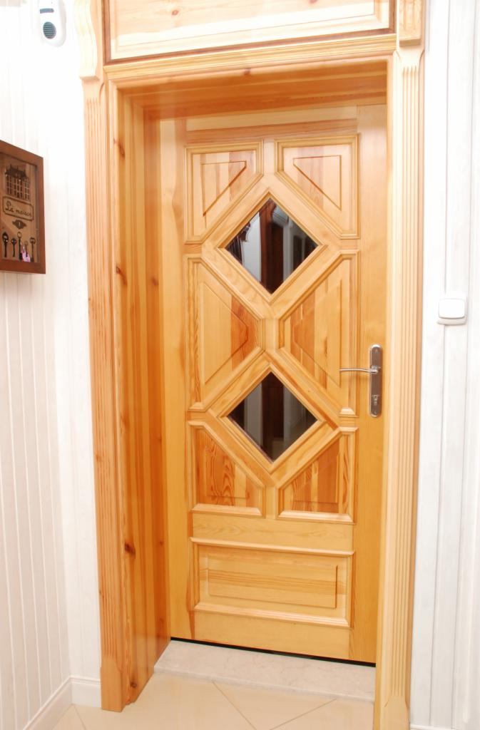 Jasna, drewniana, zdobiona drzwi wewnętrzne z dwoma romboidalnymi szybkami, osadzona w ościeżnicy z dekoracyjnymi kolumnami.