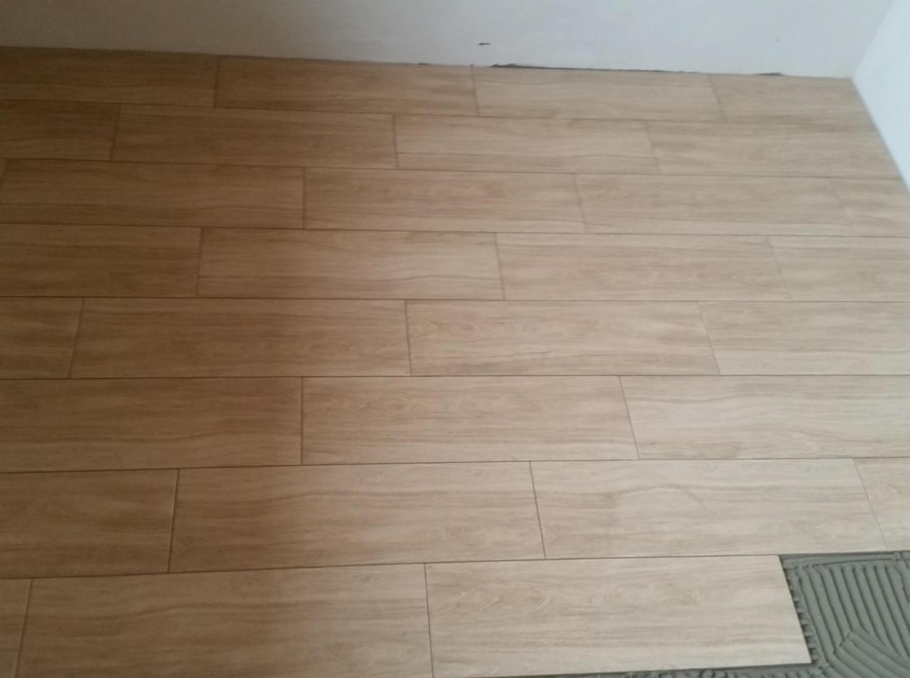 Ułożone podłużne płytki podłogowe imitujące drewno, z widoczną warstwą kleju pod ostatnią płytką.