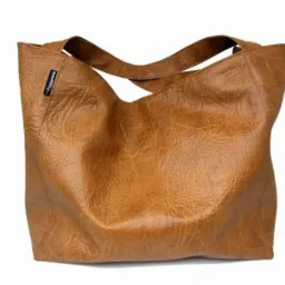 Brązowa torba shopper z imitacji skóry, widoczne przeszycia i logo na boku, na białym tle.